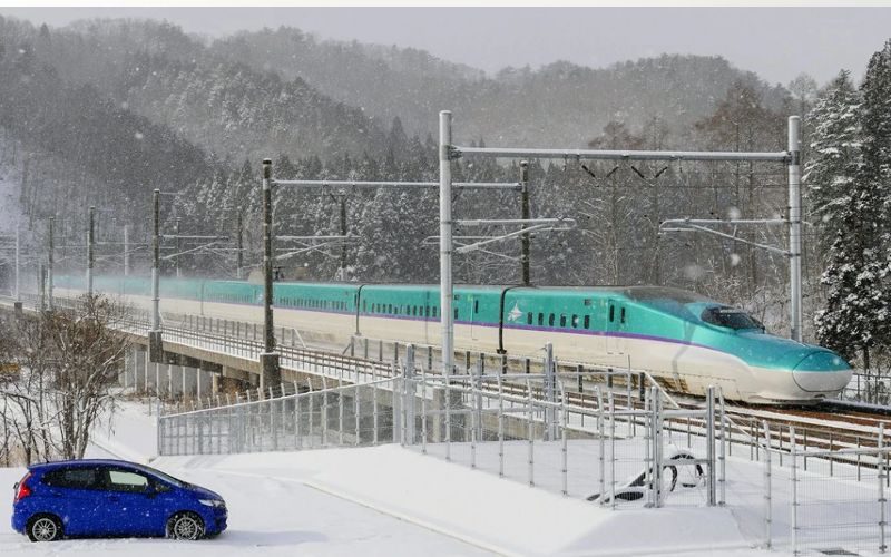 Car near the train tracks while a Hayabusa Shinkansen passes through them on a snowy day